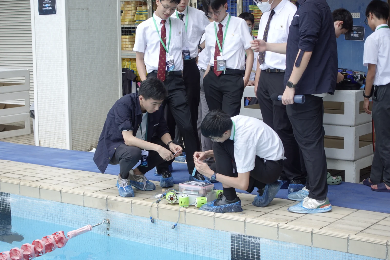 Students and a coach preparing an underwater robot beside a swimming pool